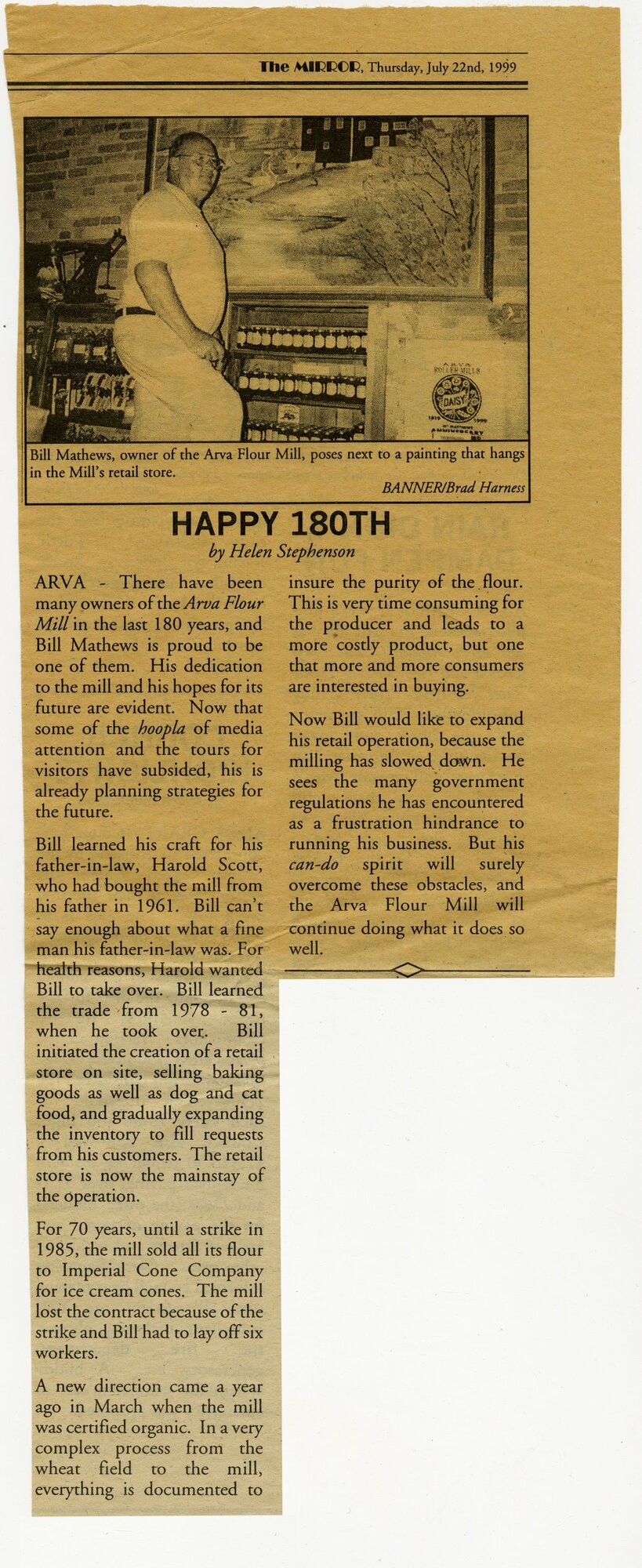 Newspaper clipping from The Mirror, July 22, 1999, headline 'HAPPY 180TH' — photo of Bill Matthews, owner of the Arva Flour Mill, standing in the retail Mill Store beside a painting of the mill