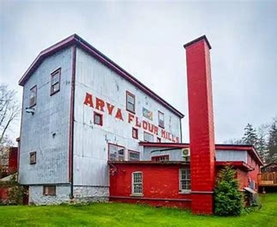 The Arva Flour Mills building — white timber cladding with ‘ARVA FLOUR MILLS’ painted across it and the red brick chimney rising alongside