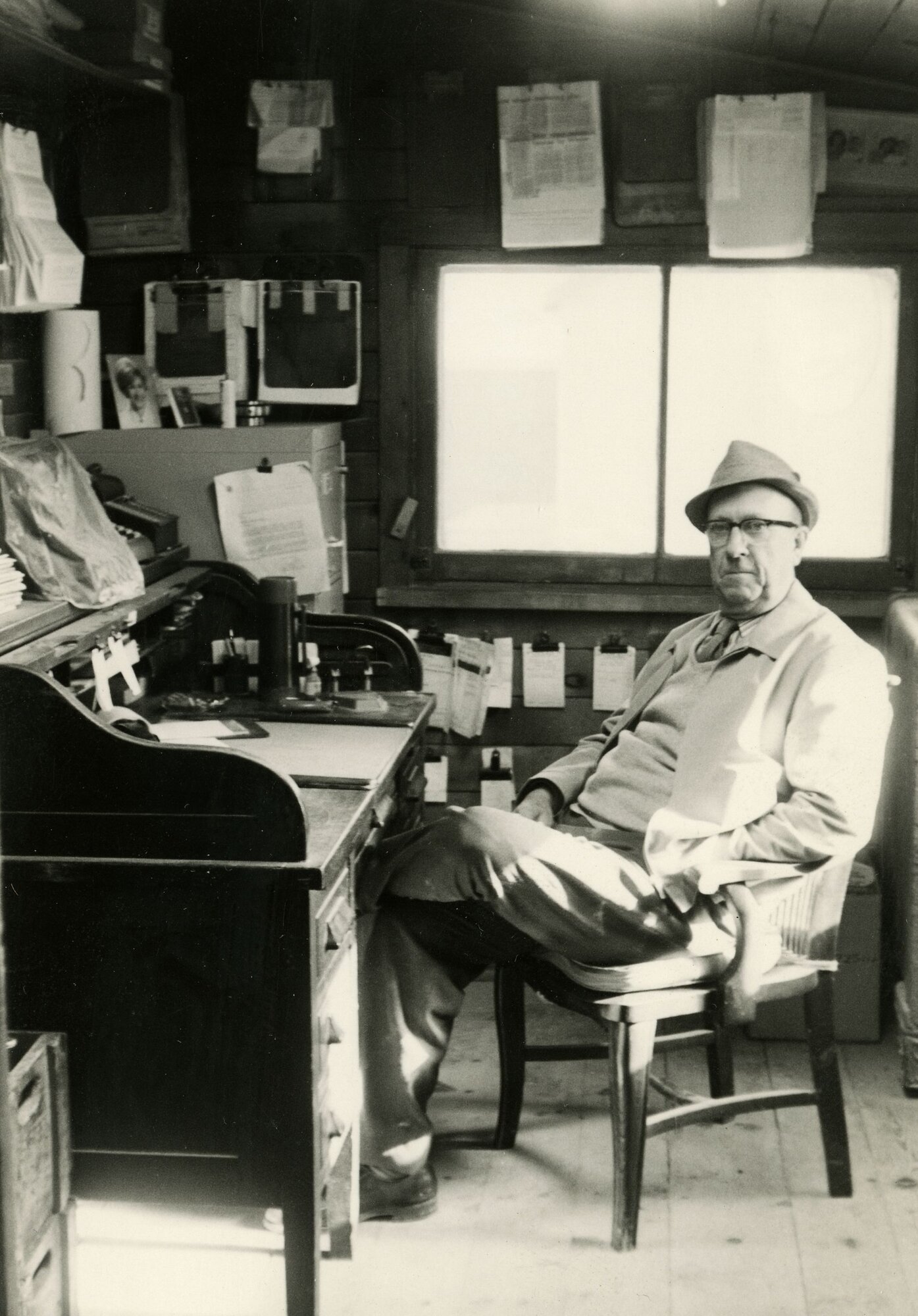 Black-and-white photograph of Harold Scott, owner of Arva Flour Mills, in a fedora seated at a roll-top desk with invoices and paperwork pinned above him on the wall