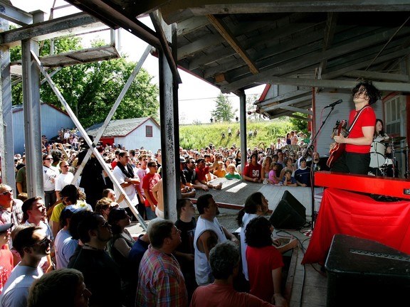 Jack White in a red shirt performing on the Arva Flour Mill loading dock on July 7, 2007, with a packed crowd of fans watching from below the dock.